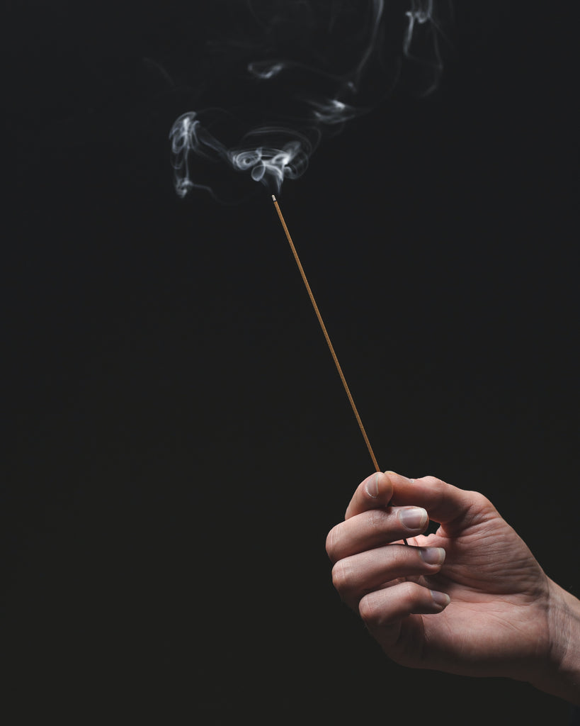 Hand holding a burning incense on a black background