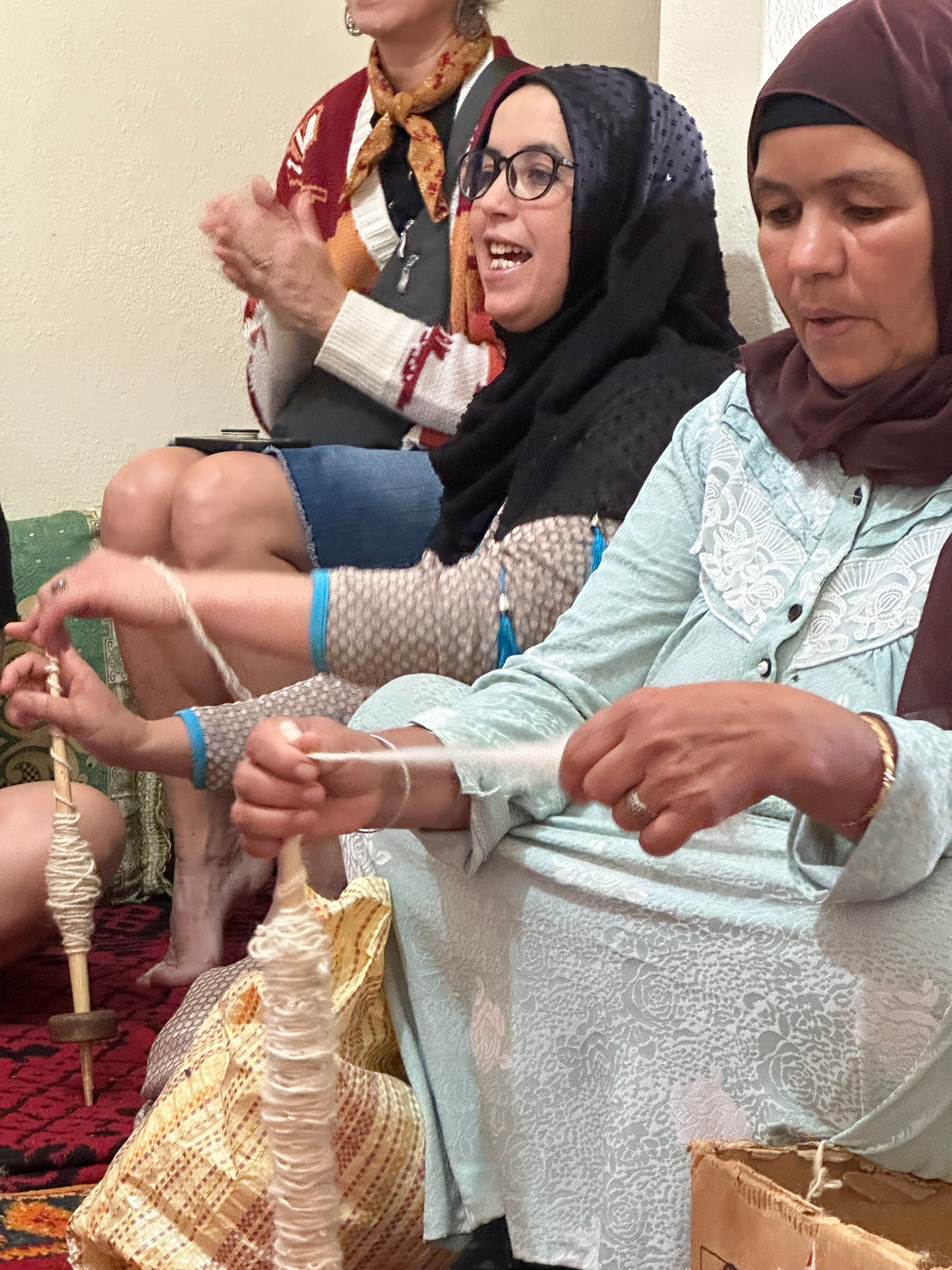 Two Moroccan women talk and laugh while winding yarn in preparation for weaving