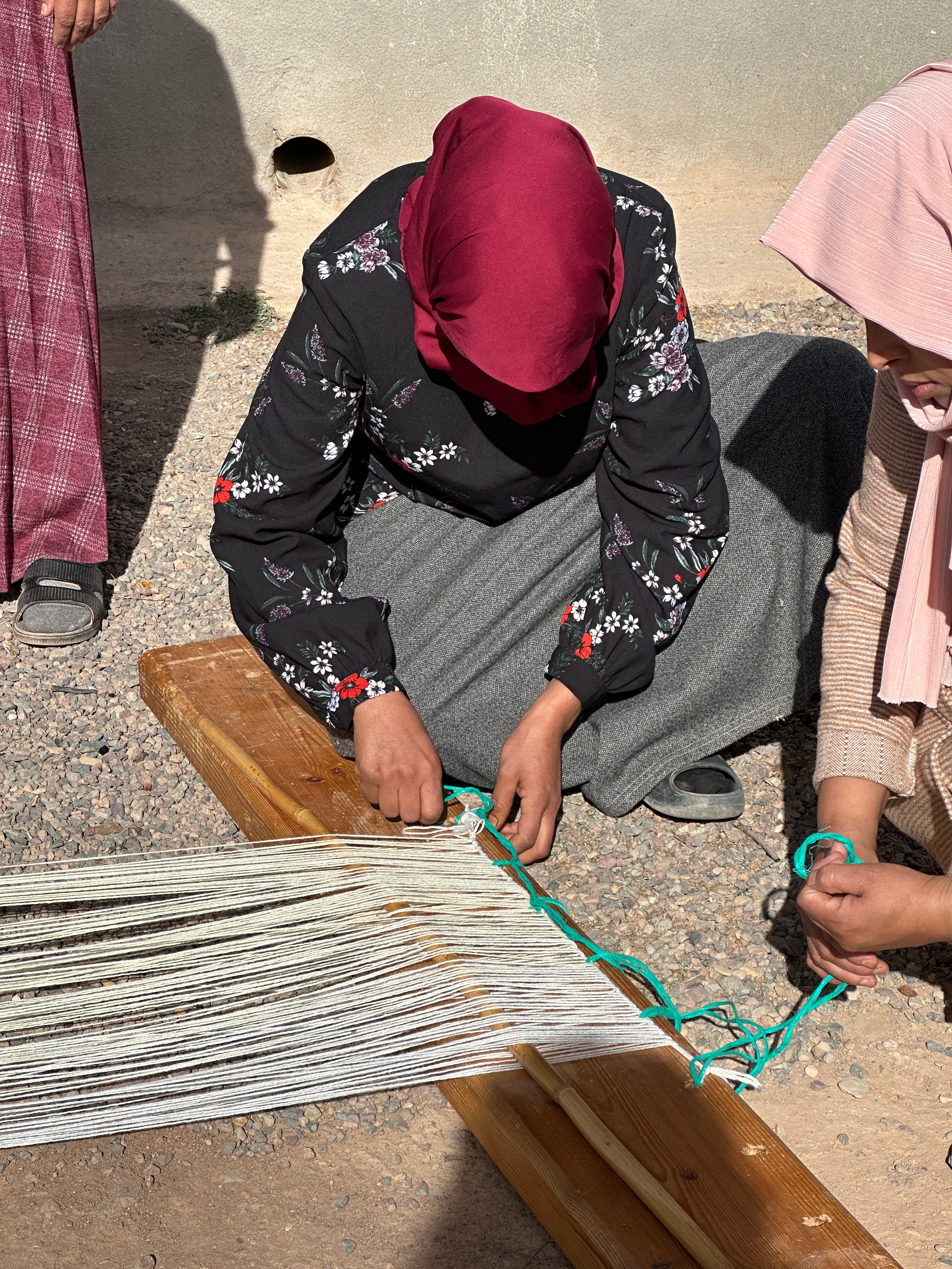 A Moroccan woman kneels on the ground to test out the quality of a warp in preparation for a new weaving.