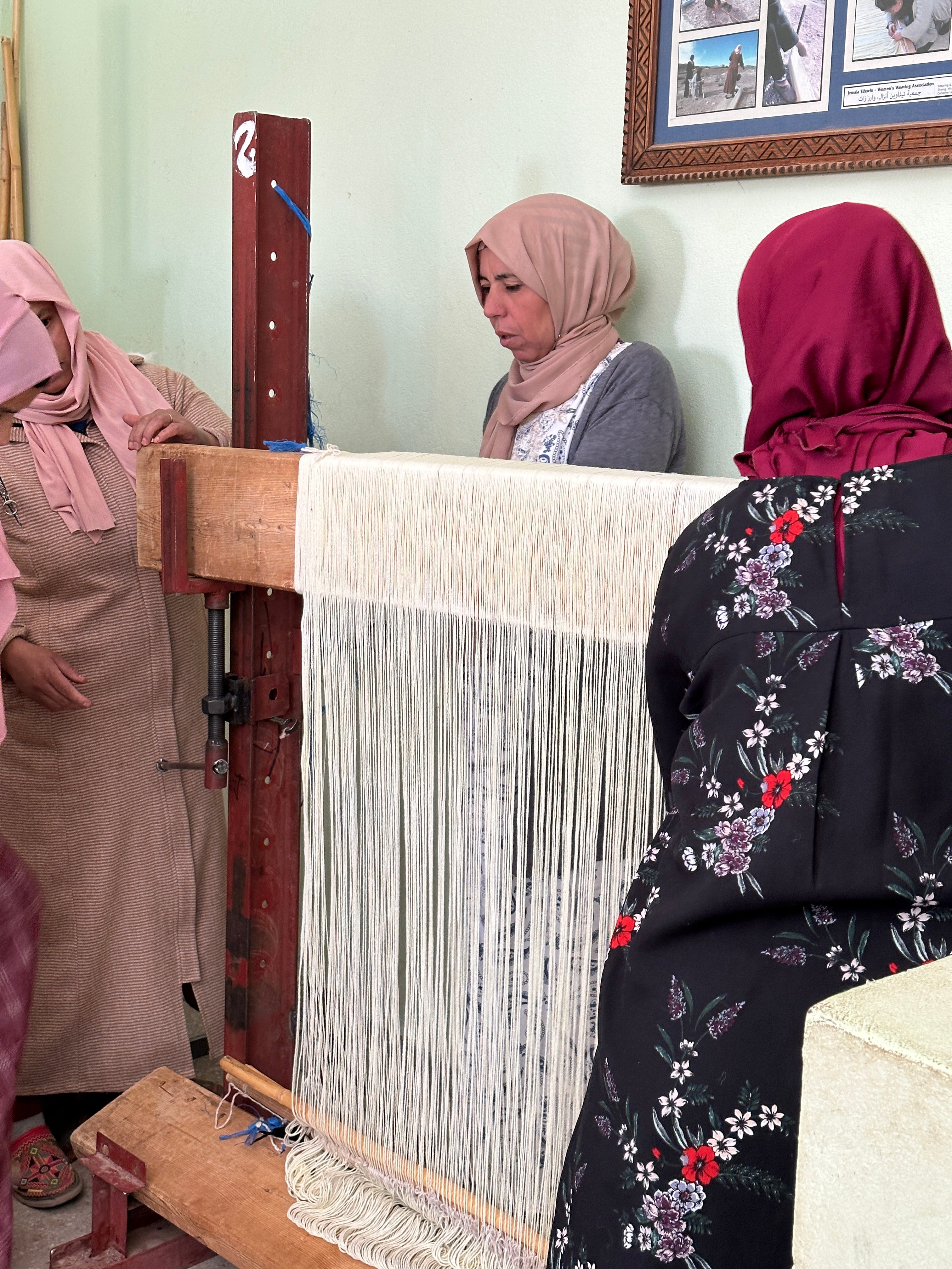 Three Moroccan work together to prepare a loom for weaving.