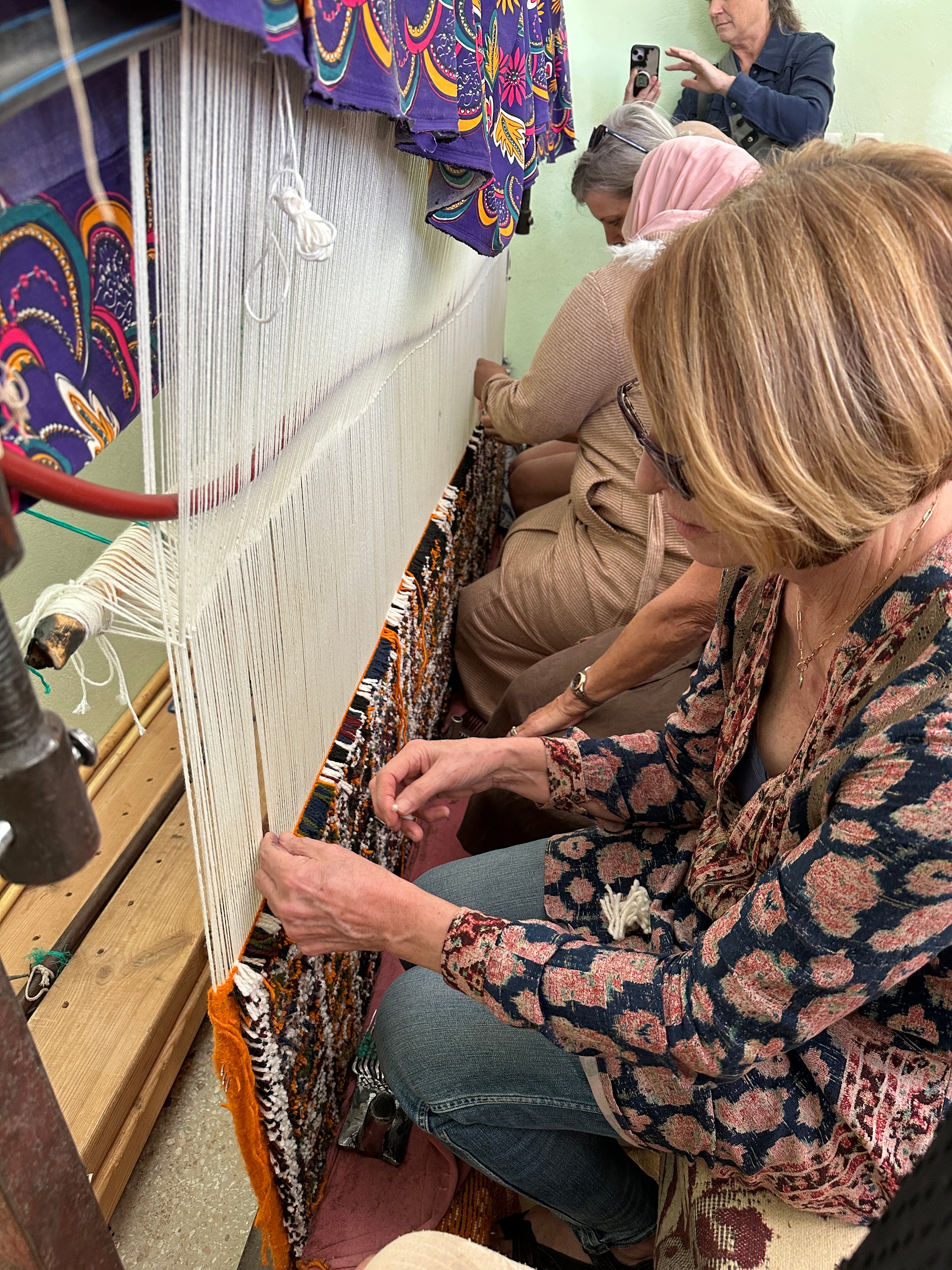 Community members and visitors work together at the loom to weave a hand knotted rug.