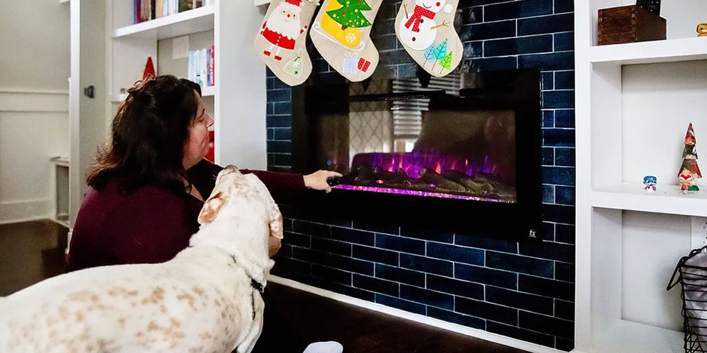 Homeowner with dog adjusting the flame and heat settings using the Touchstone Sideline 45 Smart Electric Fireplace remote control