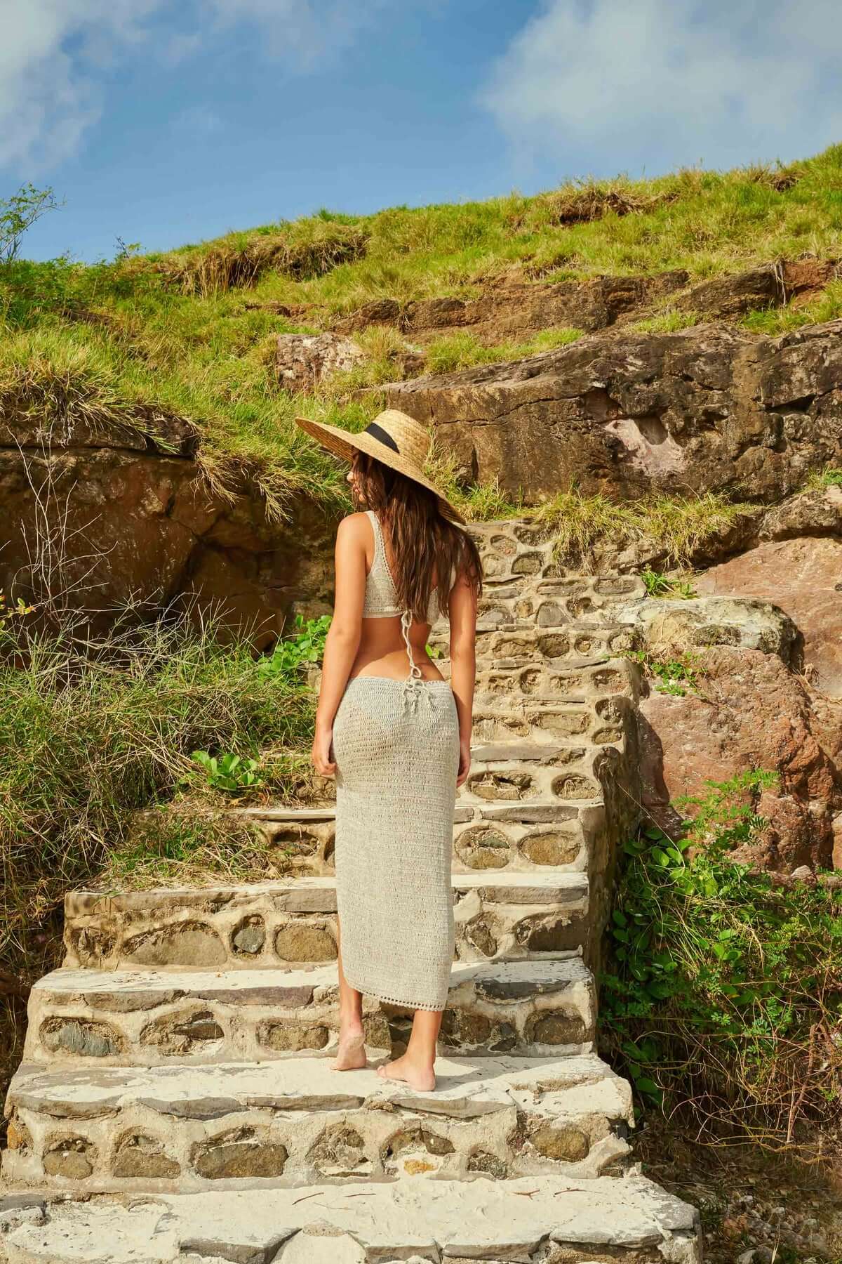 a model standing on stone steps in a beige knit cover-up set and a hat
