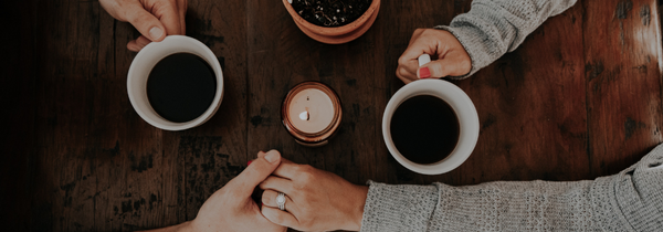 Two hands holding across a table with two cups of coffee.