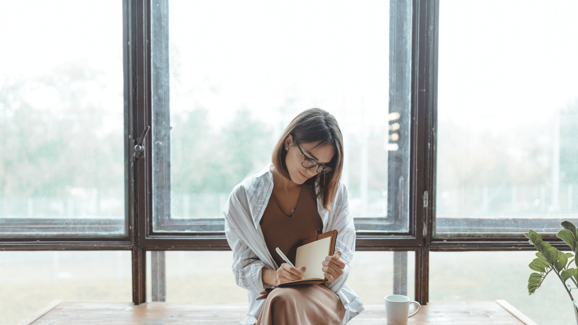 woman writing in journal in front of large window