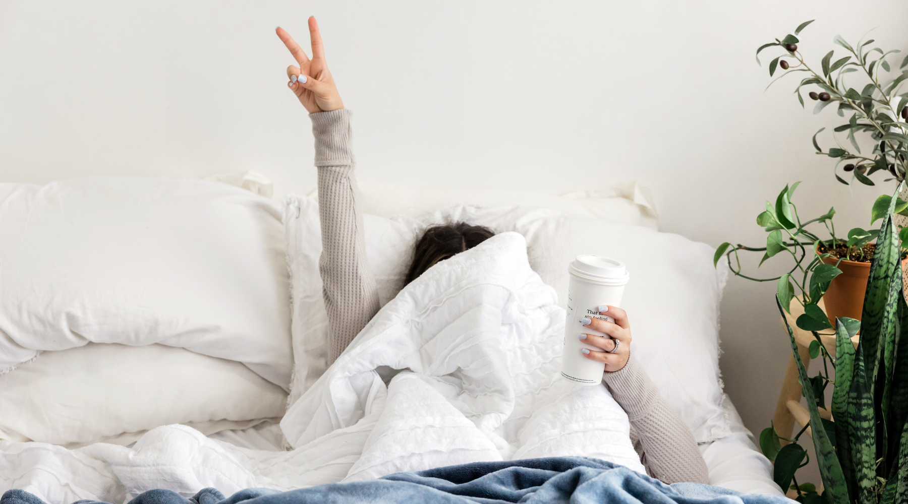 woman in bed with coffee giving a peace sign