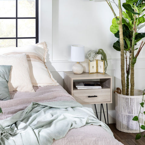 Neutral bedding on a queen bed next to a fiddle fig leaf plant and a wooden nightstand. 