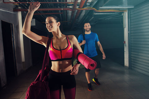 The woman is holding a yoga mat as the couple approaches the gym for their workout