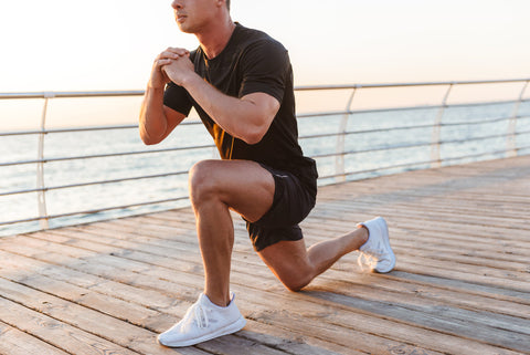 A man in black sportswear doing knee workouts in front of beach.