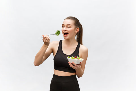 A woman wearing black sportswear posing while eating a healthy meal.