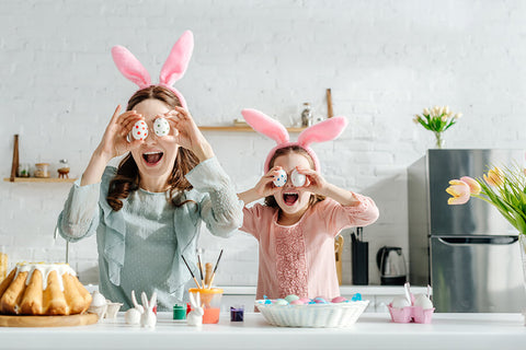 A happy mother and daughter wear bunny ear headbands and hide their eyes with Easter eggs