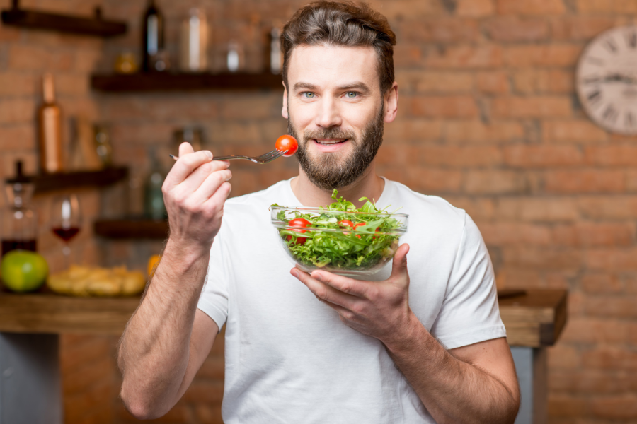 A fit man in white shirt enjoys his bowl of vegetable salad.