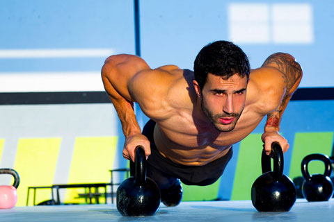 A bodybuilder does pushups using kettlebells 