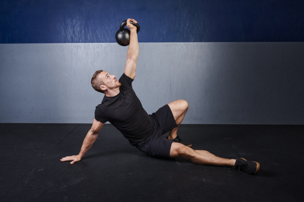 A man in black sportswear exercising using a kettlebell.