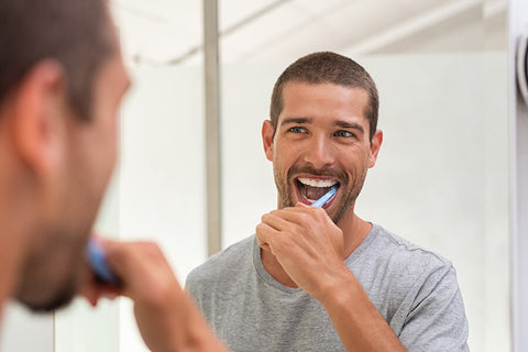 A man happily brushes his teeth while facing the mirror