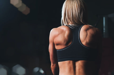 A woman in a sports bra flexes her back muscles