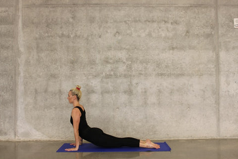 A woman in black sportswear performs a yoga pose using a yoga mat