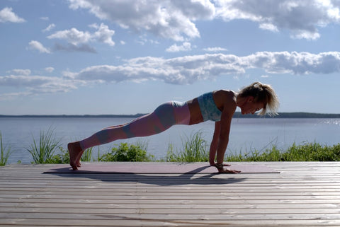 A woman in sportswear does exercise in front of a body of water