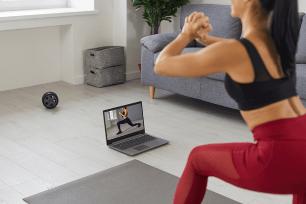 A woman in black and maroon sportswear working out using a digital video playing on her laptop.