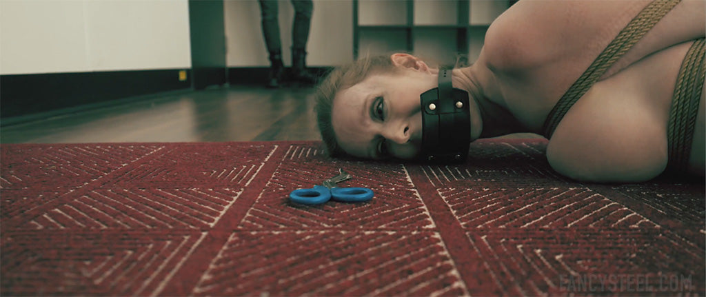 close up of a woman wearing a gag, looking at a pair of scissors on the floor