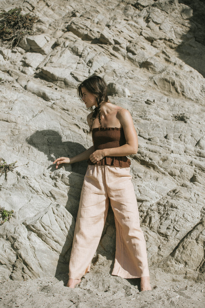 our model Becca, wearing brown top and peach pants, leaning on a big rock