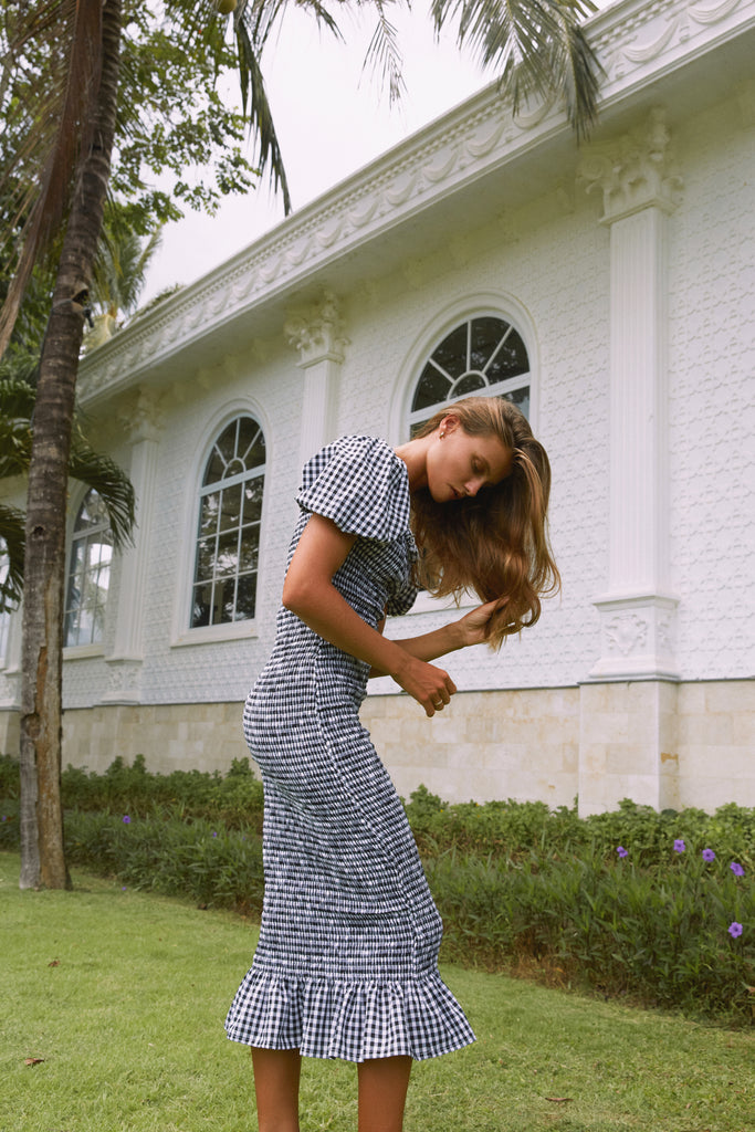 A woman wearing  Brigitte Midi Dress in Black Gingham standing in front of a house