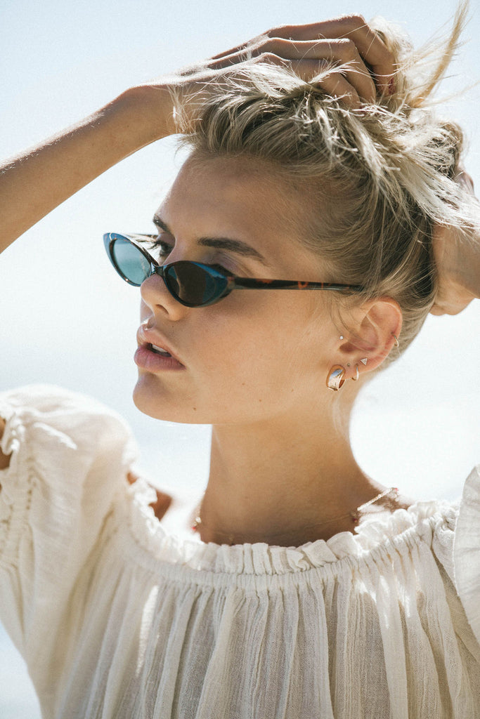 Our model Bronte wearing cream off-shoulder blouse and black sunglasses while tying her hair up