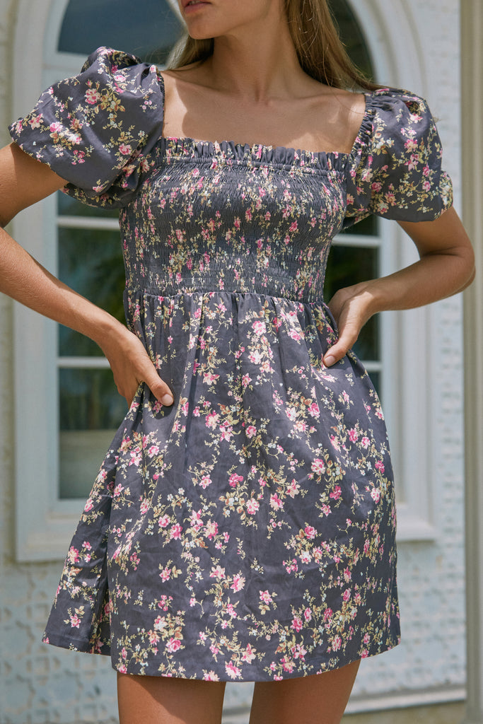 A woman in a Camille Mini Dress poses outside the house