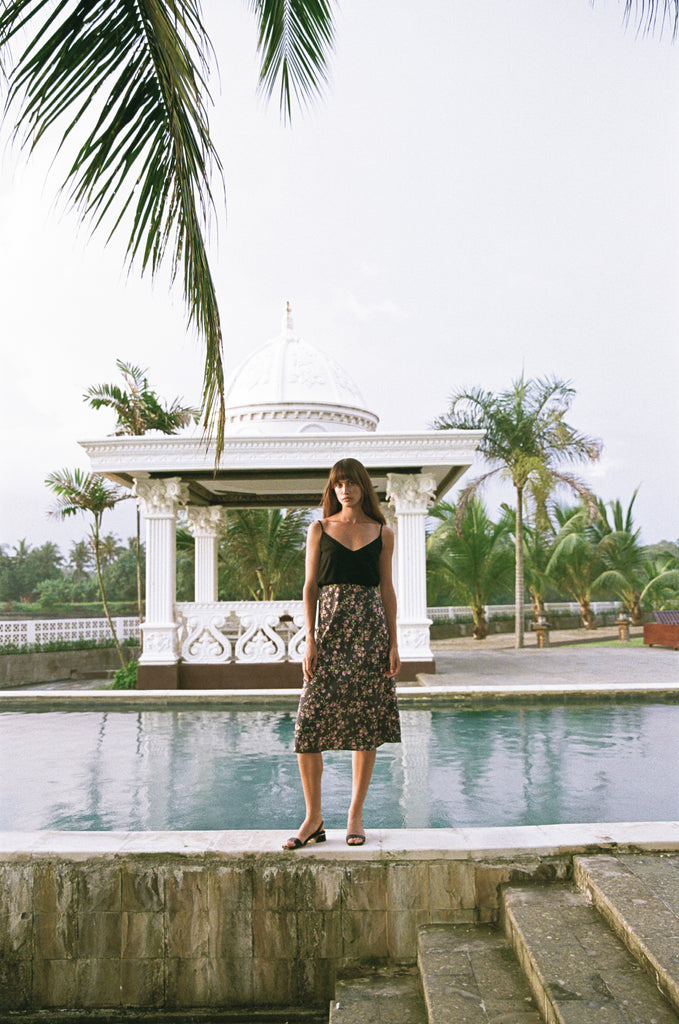 A woman waering Cora Singlet in black and a floral skirt standing next to a pool