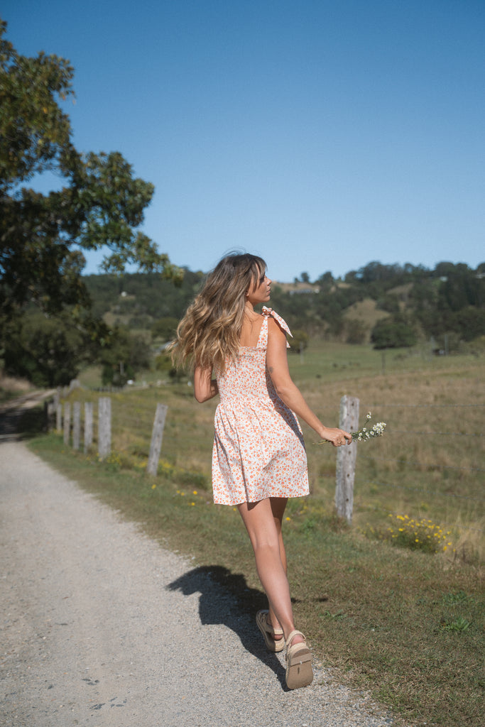 A back view image of a woman wearing tie-up dress running on a dirt road while holding flowers