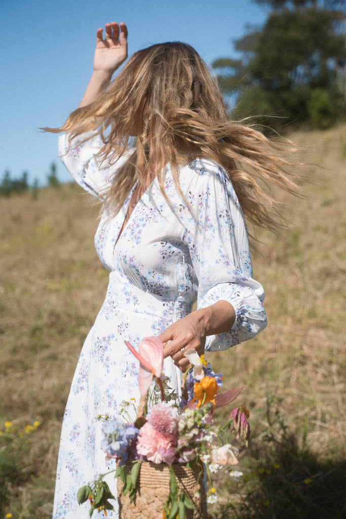 A woman wearing blue floral dress while carrying a basket of flowers