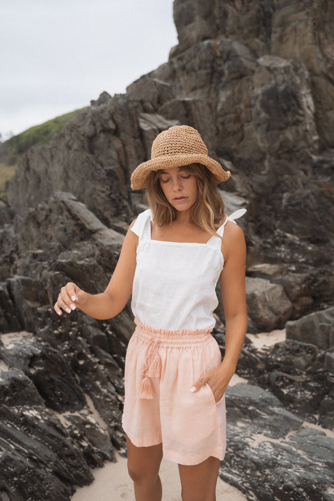 Woman wearing Stella Top in White & Luella Short and a knitted hat standing in front of big rocks