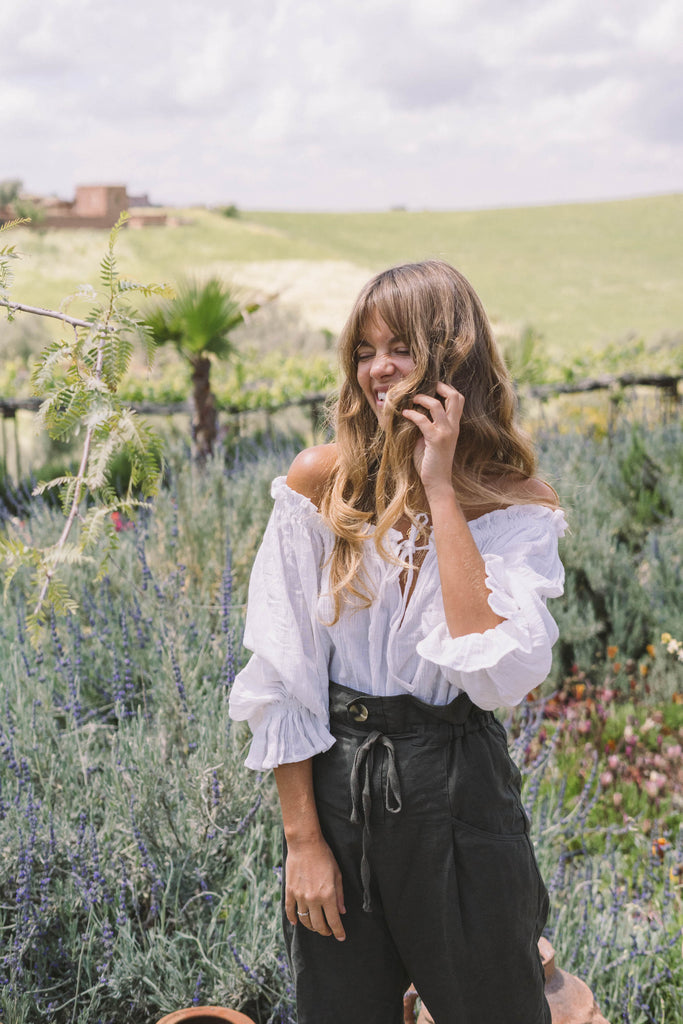 our model wearing a white off-shoulder top smiling while holding her hair