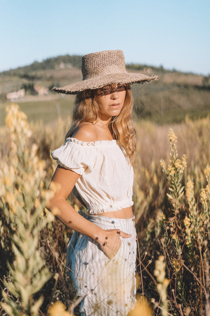 Our model modelling while standing in a grass field wearing an off-shoulder coordinates and hat