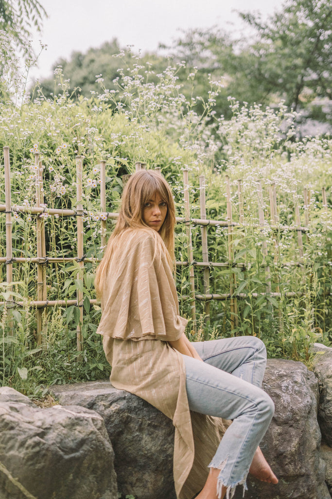 a woman wearing a kimono-like wrap dress and denim jeans while sitting on a flower garden