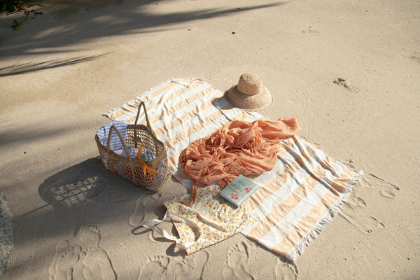 A beach blanket, a basket, and a hat on the sand