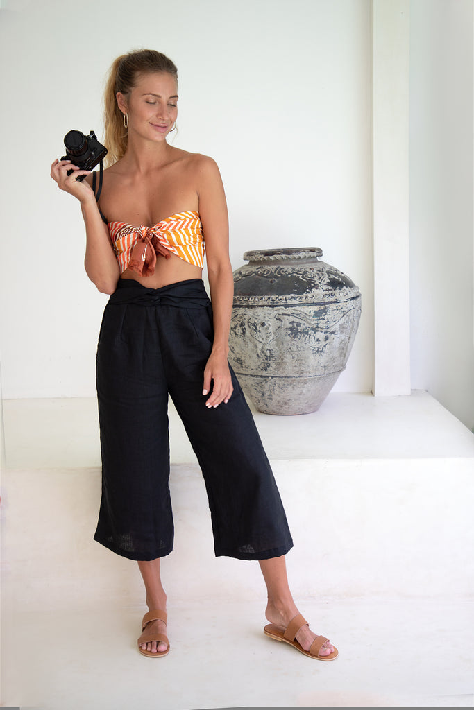 women wearing black crop linen pants and a bralette check top holding a DSLR camera