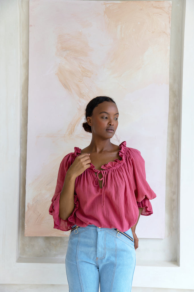 Woman wearing pink blouse standing in front of a painting