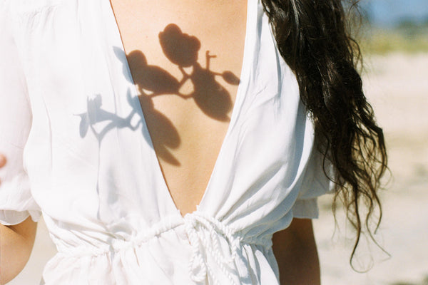 A close-up image of our model wearing a white wrap dress on a beach with an silhouette of flower 