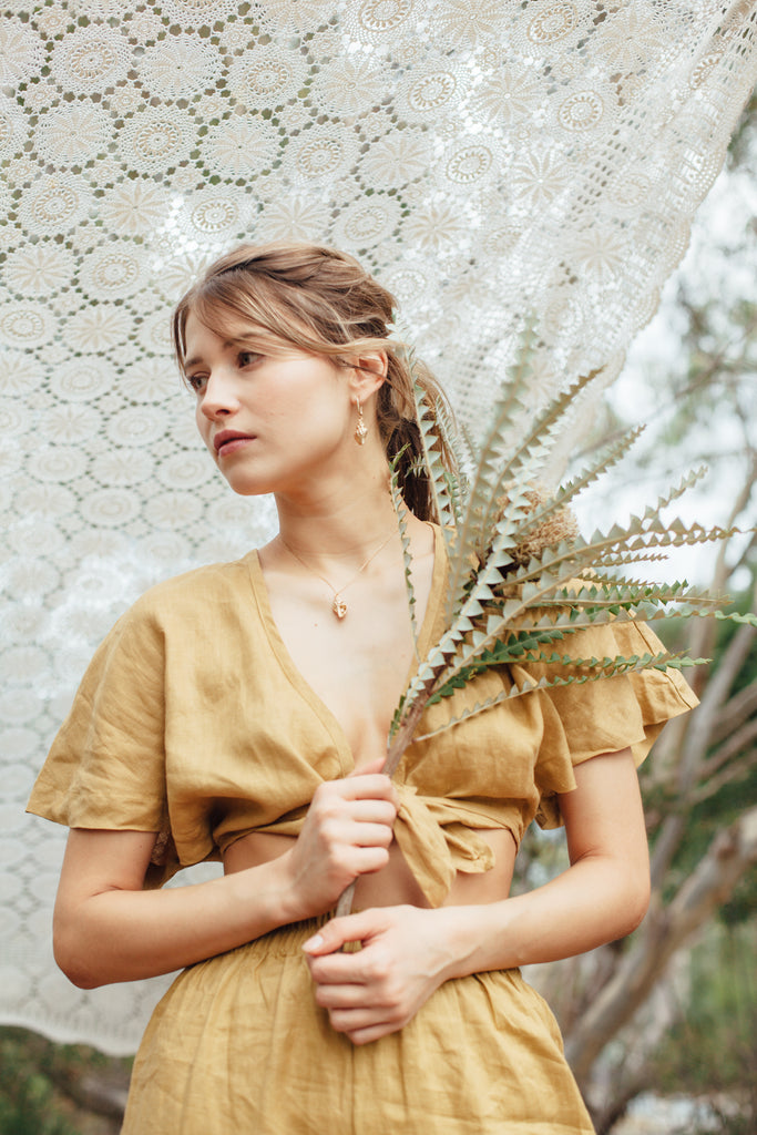 our model posing in the camera, wearing green coordinates holding a rustic piece of flower in front of a piece of white lace cloth