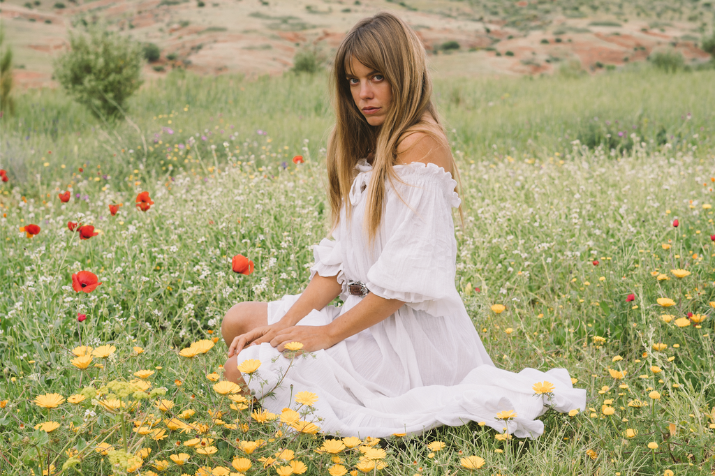 our model wearing white off-shoulder dress sitting on a field of grass and flowers 