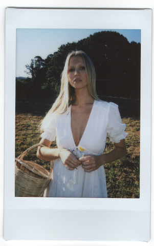 a polaroid picture of a woman wearing white dress holding a basket