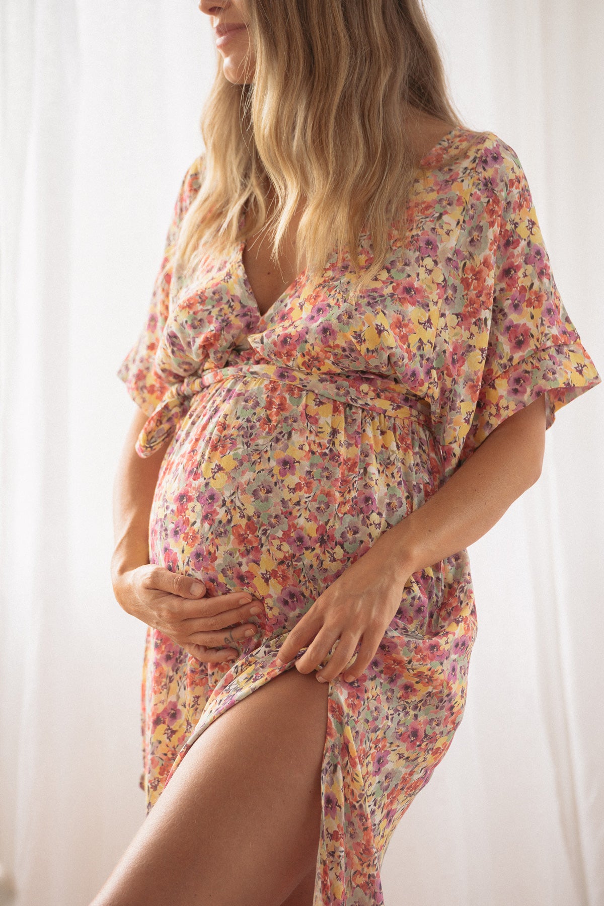 Pregnant woman wearing colourful floral print maternity dress showing off her prominent baby bump