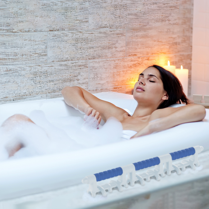 a woman relaxing in a bubble bath, with a koa massage tool