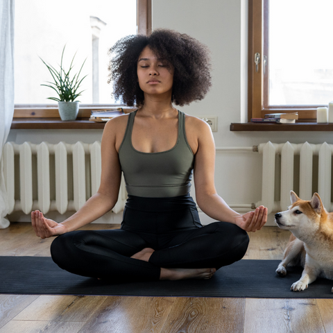 A woman sitting on the floor, meditating next to her dog at home