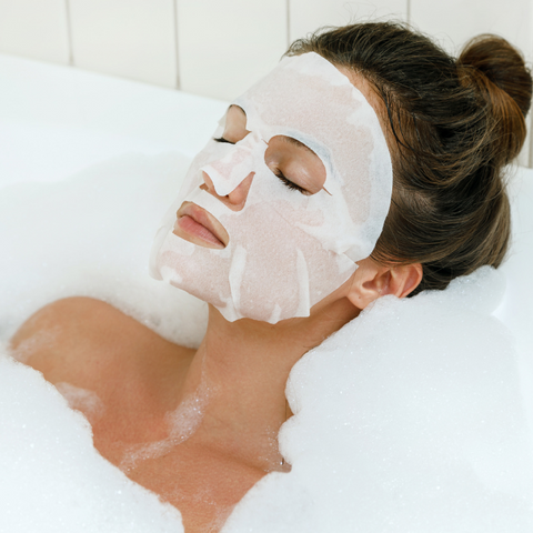 A woman relaxing in a bath with a MintBiology Tencel Sheet Mask