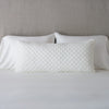 Silk Velvet Quilted Throw Pillow - Renewal | Winter White | 16x36 pillow leaning upright against white sleeping pillows and a neutral headboard.