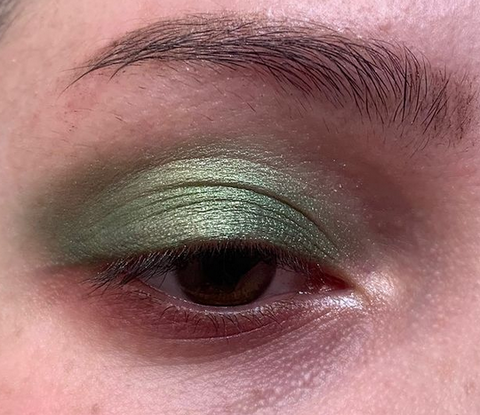 Model wearing green shimmery eyeshadow with minimal brows and lashes