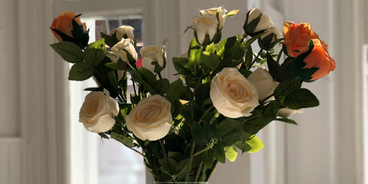 Vase with white and orange artificial flowers in sunlight