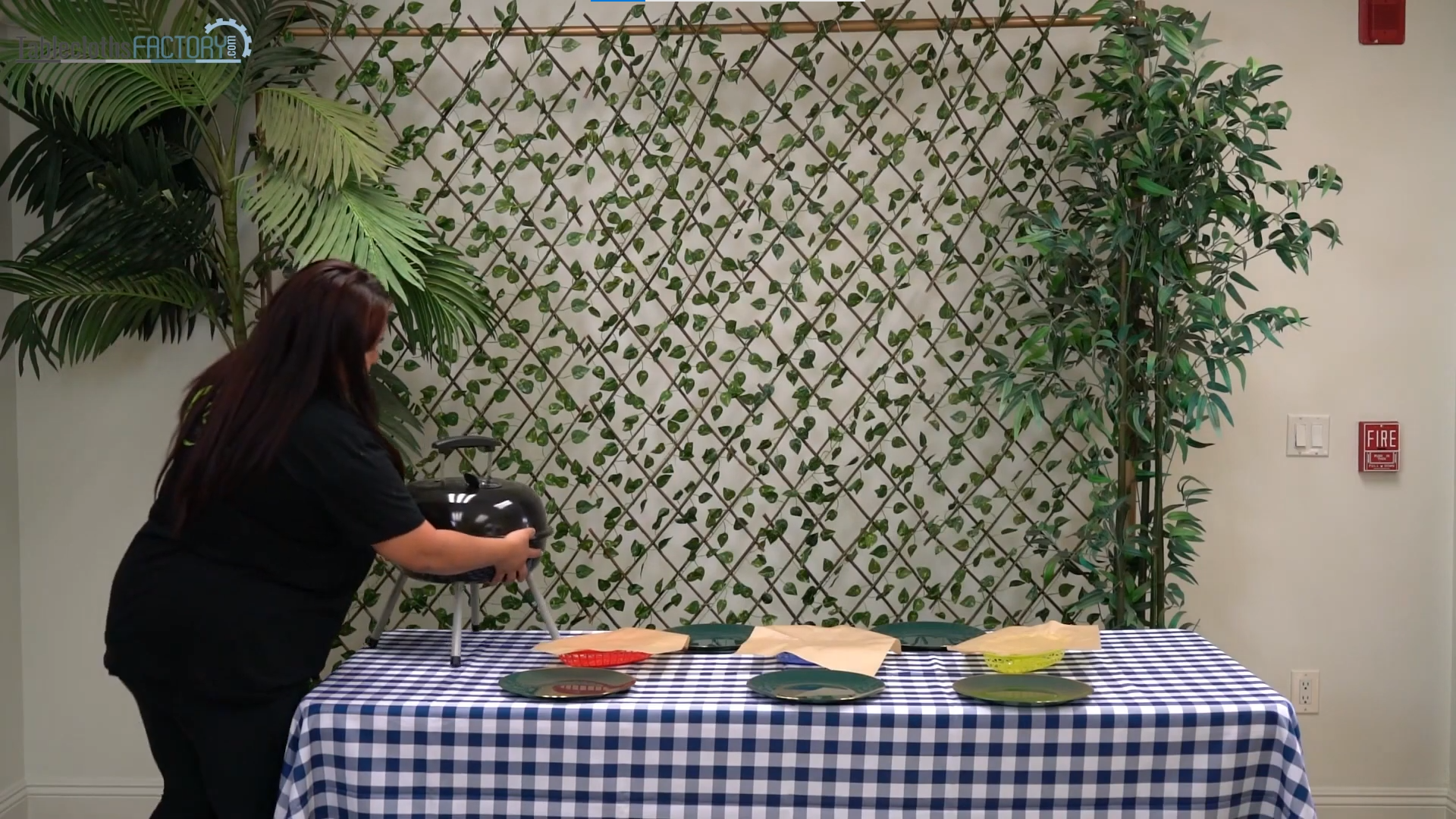 Woman setting a white/blue plaid tablecloth and dinner plates on the table